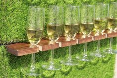 wine glasses are lined up on a wooden shelf in front of green moss covered wall