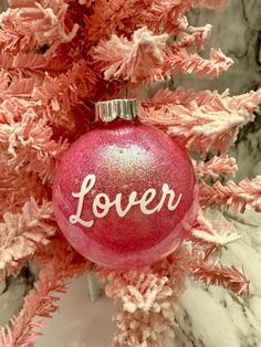 a pink ornament with the word lover on it hanging from a christmas tree