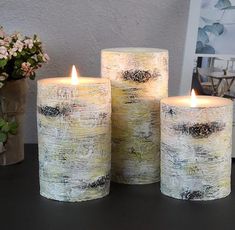 three lit candles sitting on top of a table next to a vase with flowers in it