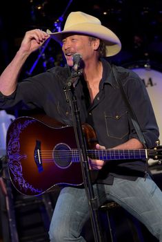 a man wearing a cowboy hat singing into a microphone and holding a guitar in his right hand