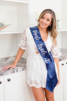 a beautiful young woman wearing a blue sash standing in front of a white counter top