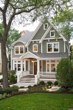 a gray house with white trim and two story windows on the second floor is surrounded by trees