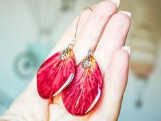 a pair of red flower shaped earrings on a person's hand