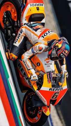 a man riding on the back of a motorcycle down a race track in an orange and white outfit