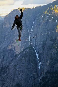 a man on a rope high up in the air with mountains and trees behind him