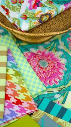 many different colored fabrics are stacked on top of each other in a basket and one has a blue bird perched on it