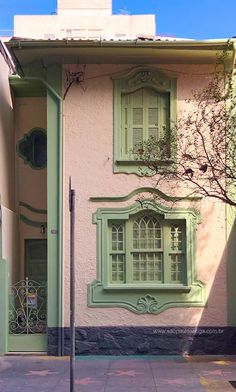 a pink house with green shutters and a tree in front of the door is shown