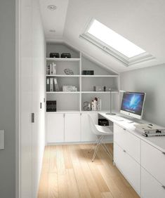 a room with a desk, computer monitor and bookshelf in the corner under a slanted skylight