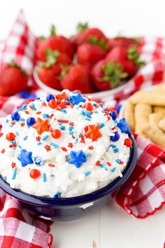 red, white and blue cake in a bowl on a checkered tablecloth with strawberries