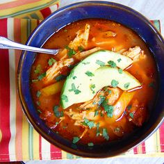 a bowl of chicken tortilla soup with avocado and cilantro