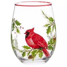 a red bird sitting on top of a glass filled with holly and pineconis