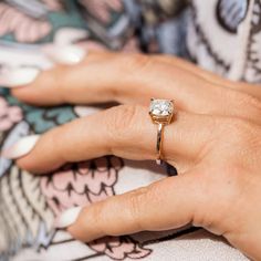 a woman's hand wearing a gold ring with a diamond on it and a floral print shirt