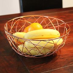 a wire basket filled with bananas and oranges on top of a wooden table next to a black chair