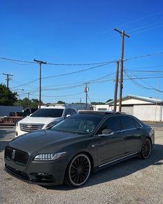 a grey car parked in a parking lot next to other cars and power lines on a sunny day