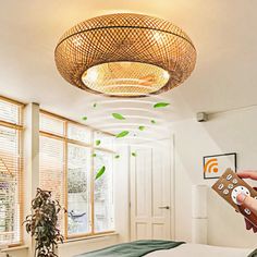 a person holding a remote control in front of a bed with green leaves on the ceiling