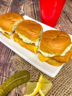 three sandwiches with cheese and pickles on a white plate