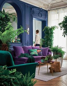 a living room filled with purple couches and lots of greenery on the walls