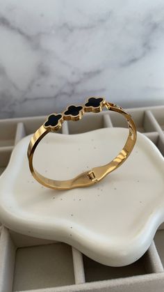 ✨Elevate your elegance with this exquisite gold bangle, a masterpiece that combines sophistication and sensuality. ✨Crafted with sleek gold and adorned with delicate black enamel clover motifs, this bracelet adds a touch of luxury to any ensemble. ✨The glimmering gold catches the light with every movement, while the bold clovers symbolize grace and allure. ✨A subtle diamond accent adds a hint of sparkle, making this piece the perfect companion for both day and night. Slip it on, and feel the confidence that only comes from wearing a truly captivating accessory. Elegant Black Bangle Gold Bracelet, Black Gold-plated Bracelets, Elegant Black Gold Bangle Bracelet, Timeless Black Bangle Jewelry, Elegant Black Bangle Bracelet, Elegant Black Enamel Bangle Cuff Bracelet, Elegant Black Enamel Cuff Bracelet Bangle Style, Elegant Black Enamel Bangle Bracelet, Elegant Black Enamel Cuff Bracelet