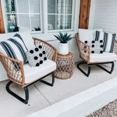 two wicker chairs with black and white pillows sitting on the front porch next to each other