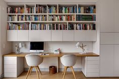 two white chairs sitting at a desk in front of a book shelf filled with books