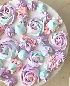 a white plate topped with lots of different colored frosting flowers and seashells