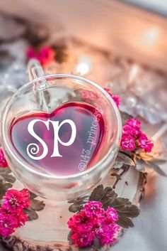 a heart shaped glass with the letter m on it and some pink flowers around it