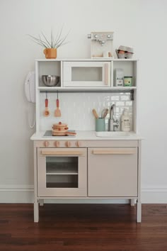 a white play kitchen with wooden floors and shelves on the wall next to an oven