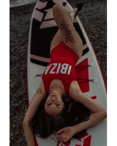 a woman laying on top of a red and white surfboard