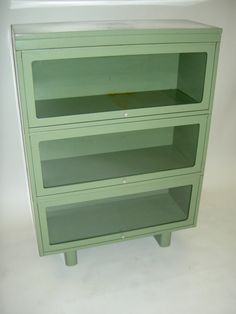 a green cabinet sitting on top of a white floor next to a shelf with two shelves