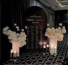 tall vases filled with white flowers and lit candles are on display in front of a black backdrop