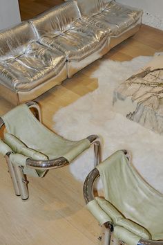 two leather chairs sitting on top of a hard wood floor next to a silver couch