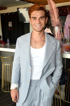 a man with red hair wearing a blue suit and white t - shirt smiles at the camera