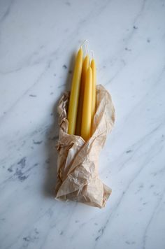 three yellow candles sitting on top of a white marble counter next to a brown paper bag