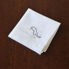 a white napkin with a bird embroidered on it sitting on top of a wooden table