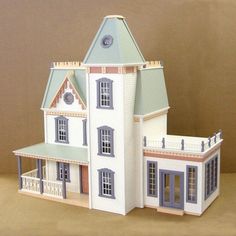 a white doll house sitting on top of a table next to a brown wall with a clock