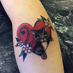 a black and white cat sitting on top of a red heart with flowers around it