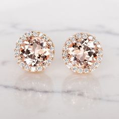 This chic pair of studs features natural pink morganites surrounded by halos of vibrant, natural diamonds. The morganites are a beautiful blush color reminiscent of rosé, and their well executed round cuts display gorgeous sparkle. The 14k rose gold settings blend perfectly with the peach morganite while the contrasting white diamonds make the rosey color of the morganite pop! Rich in color and lively sparkle, these earrings have a timeless air of elegance and sophistication. Whether you are buy Cushion Halo Earrings Rose Gold, Luxury Rose Gold Halo Earrings, Filigree Wedding Band, Vintage Engagement Ring Settings, Morganite Earrings, Rose Gold Halo, Rose Gold Earrings Studs, Peach Morganite, Blue Diamond Ring