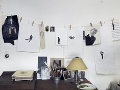 a desk with many pictures hanging on the wall and a lamp next to it,