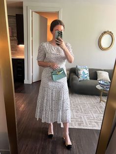 a woman taking a selfie in her living room while wearing a dress and heels