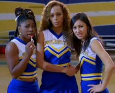 three girls in cheerleader outfits posing for the camera with one girl brushing her teeth