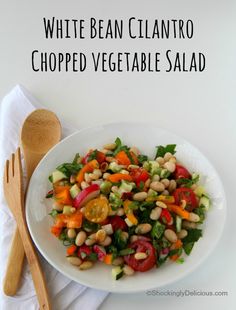 a white plate topped with salad next to a wooden spoon