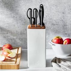 an assortment of kitchen utensils in a holder on a counter next to apples