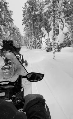 two people on snowmobiles going down a snowy road with trees in the background