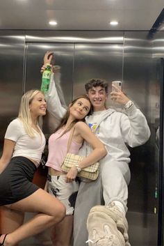 three people taking a selfie in front of an elevator with one person holding up a cell phone