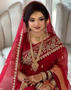 a woman in a red and gold bridal outfit sitting on a white couch with her hands together