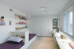 a bedroom with white walls and purple bedspread on the bottom bunk, along with shelves filled with books