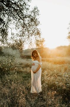 a pregnant woman standing in a field at sunset