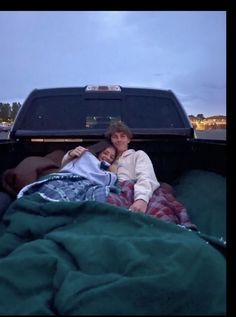 two people laying in the back of a pick up truck with blankets on it's bed