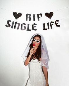 a woman wearing sunglasses and a veil holding a lollipop in front of a sign that says rip single life