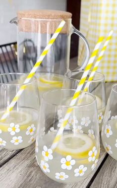 four glasses with lemonade and straws in them sitting on a table next to a pitcher